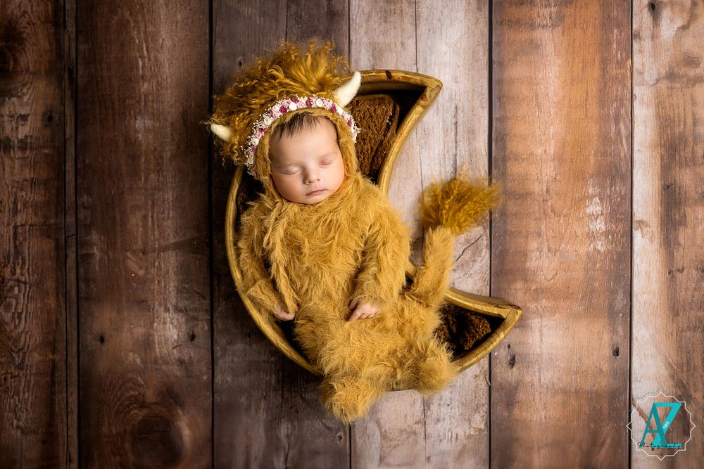 Creative newborn photography with cozy gold knit outfit and wooden backdrop.