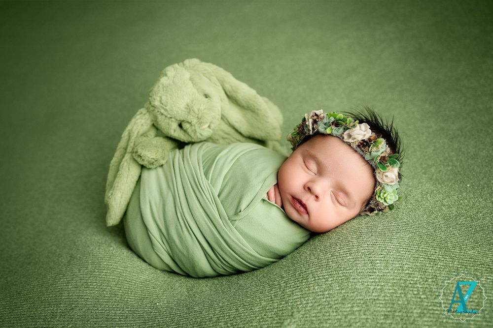 Peaceful sleeping newborn wrapped in mint green with floral crown on textured backdrop.