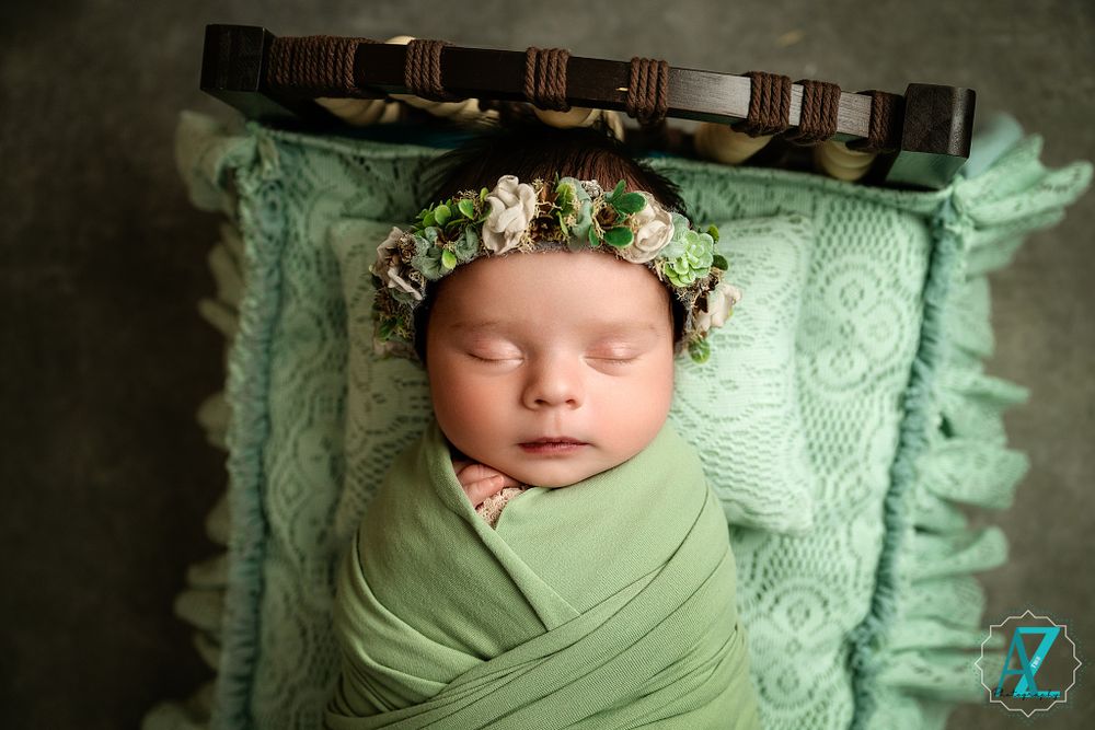 Delicate newborn photography with floral crown and mint green wrap on textured pillow.