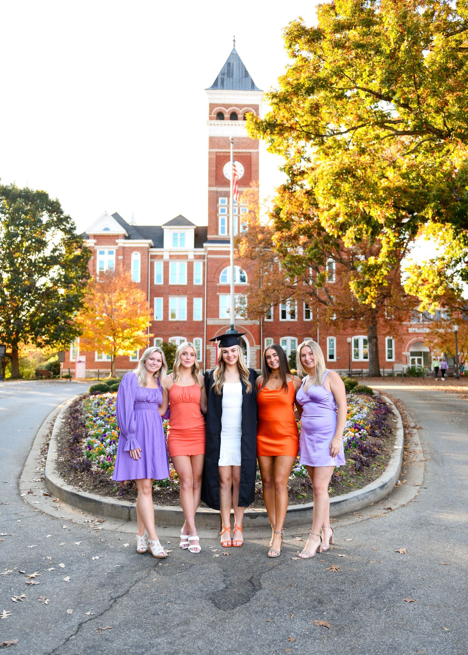 Group photo in front of brick clock tower with people wearing orange and purple dresses.