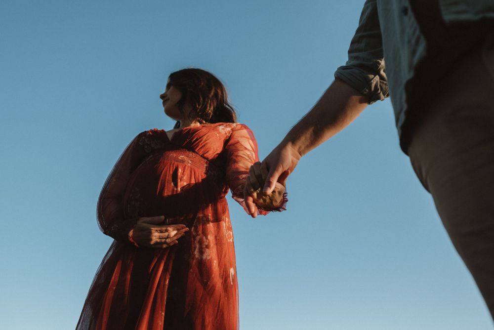 Dancing in the sun with flowing red dress against blue sky.