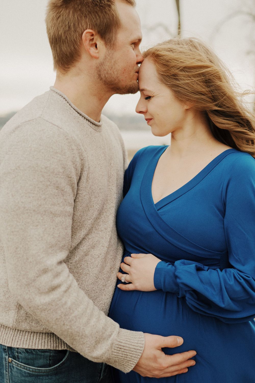 A romantic maternity photo of a couple embracing outdoors against a bright background.