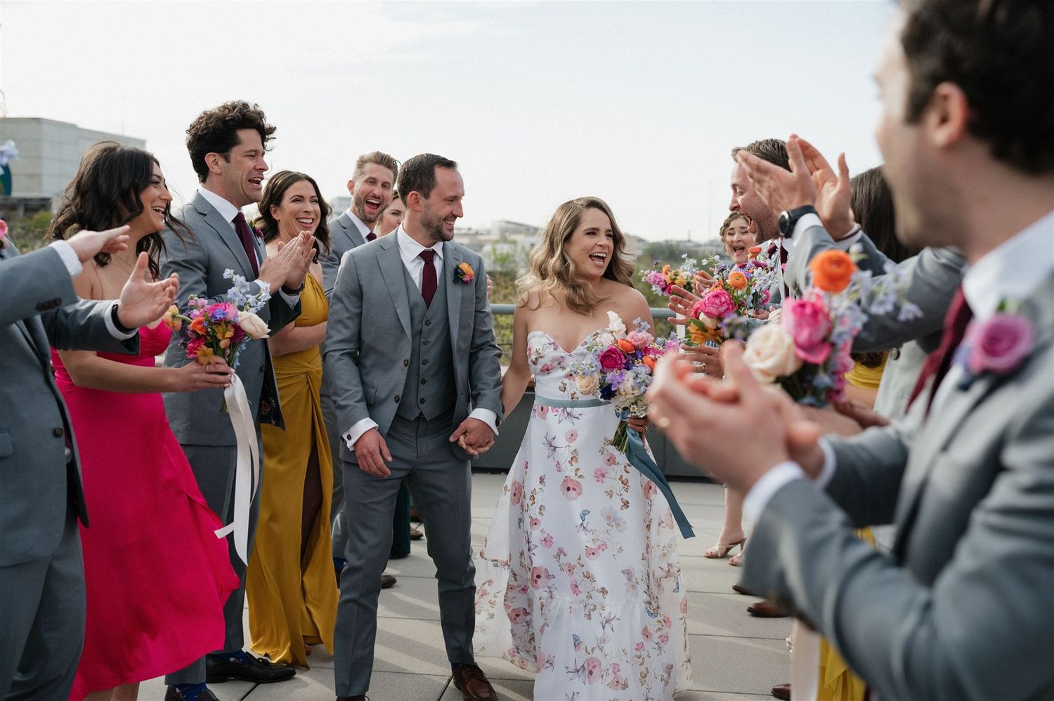 Wedding guests line up and cheer along a pathway as newlyweds walk through during an outdoor celebration.