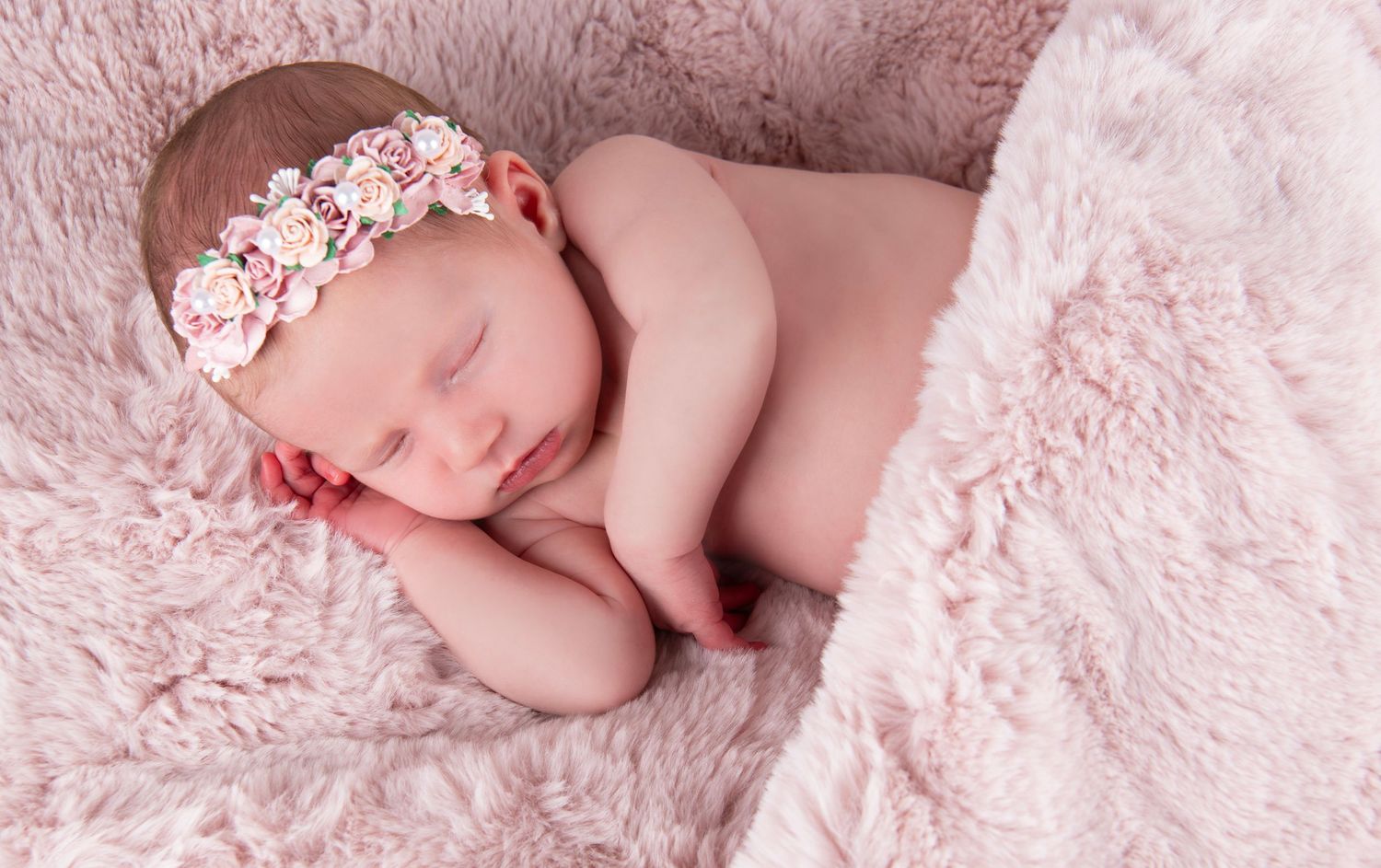 Newborn sleeping on pink fur blanket wearing floral headband.