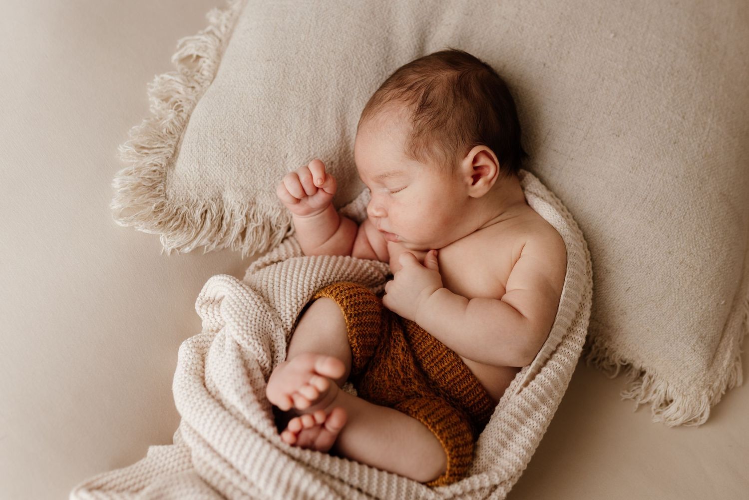 Peaceful sleeping newborn nestled in cozy cream-colored knit textures.
