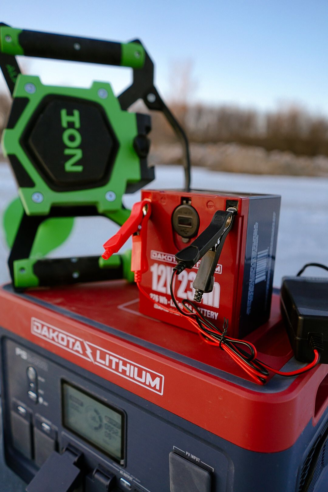 Green work light and red Dakota Lithium power station setup on icy surface.