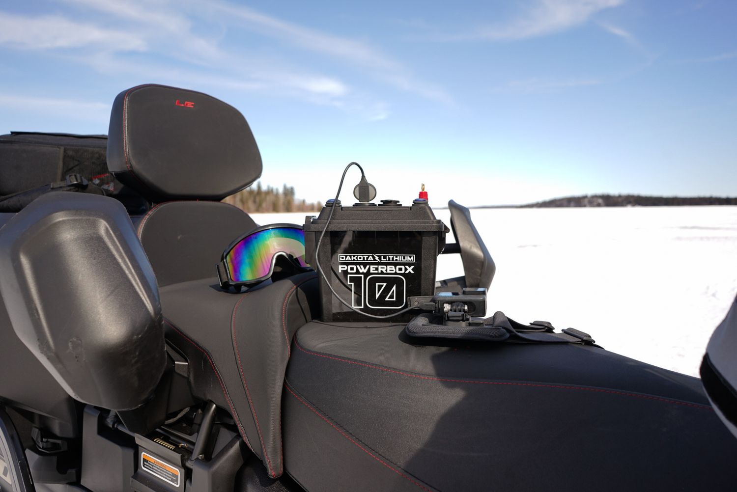 Power station mounted on snowmobile seat with blue sky and winter landscape visible.