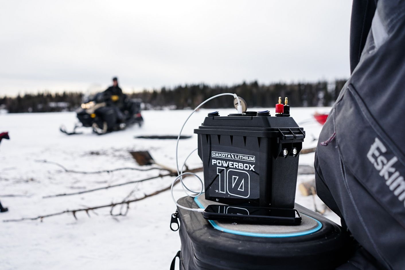 Portable power bank mounted on snowmobile with another vehicle visible in distance on snowy terrain.