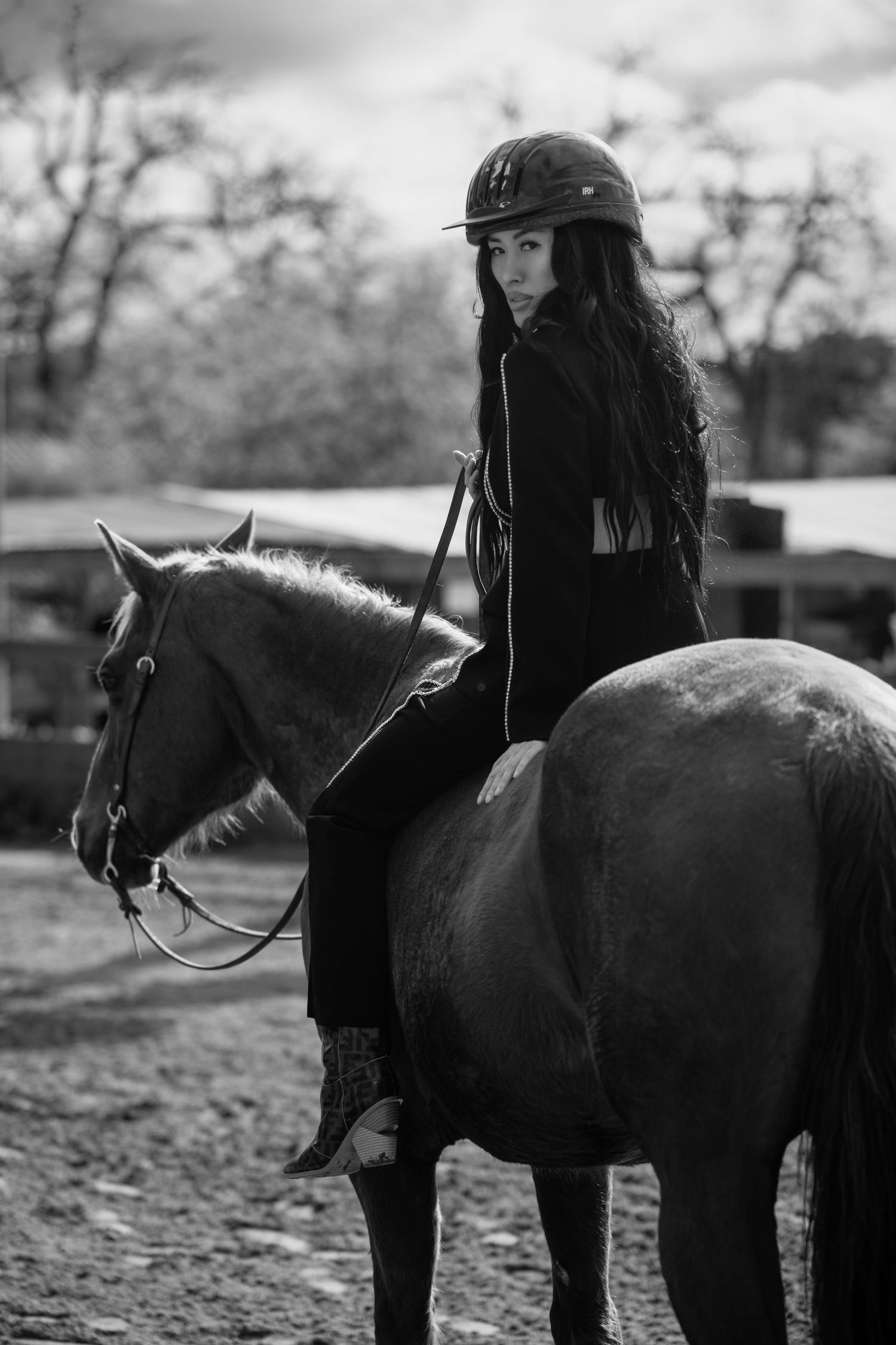 A rider in dark attire sits atop a brown horse in a black and white photograph outdoors.