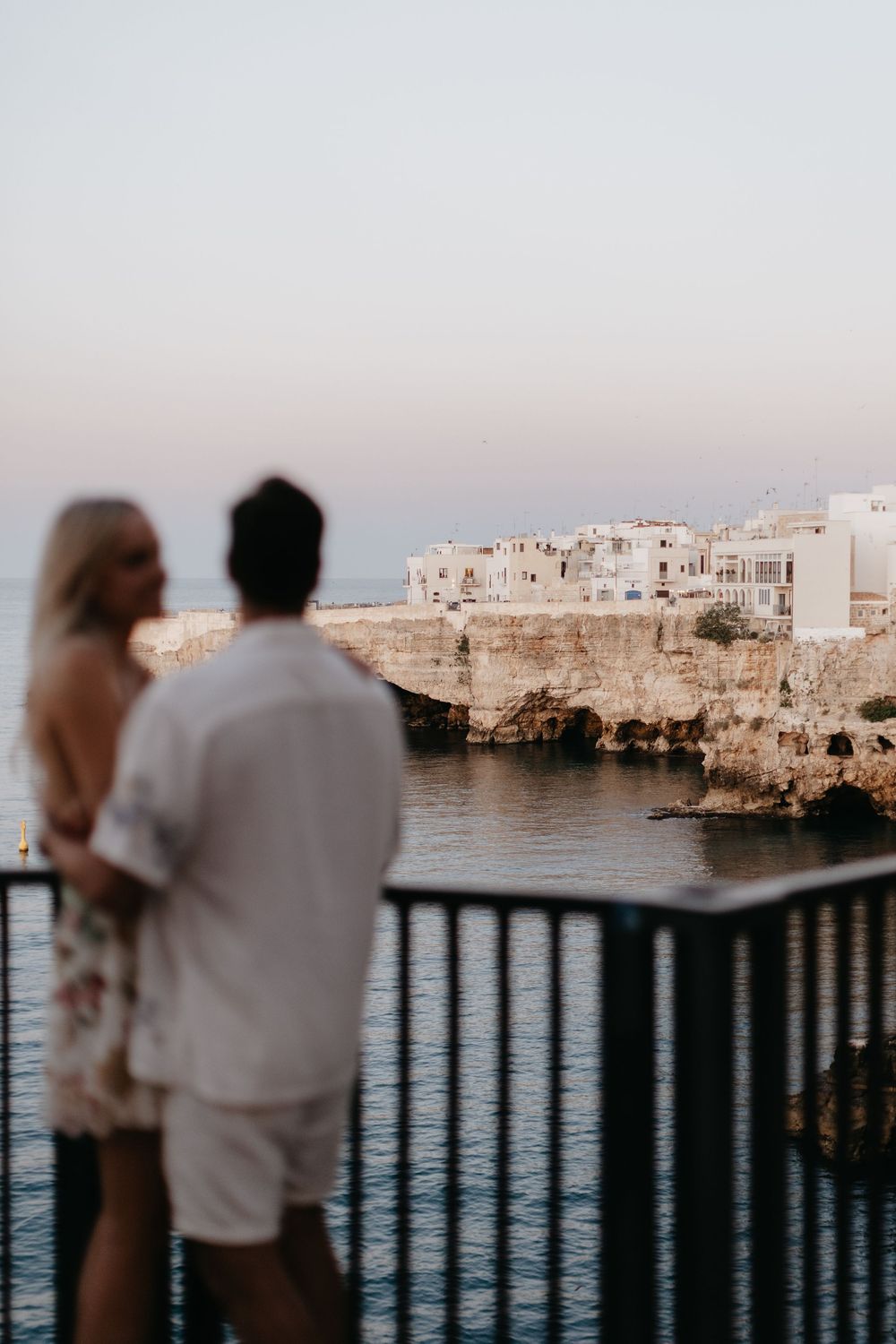 Couple overlooking a scenic Mediterranean coastal town with white buildings and blue waters at sunset.