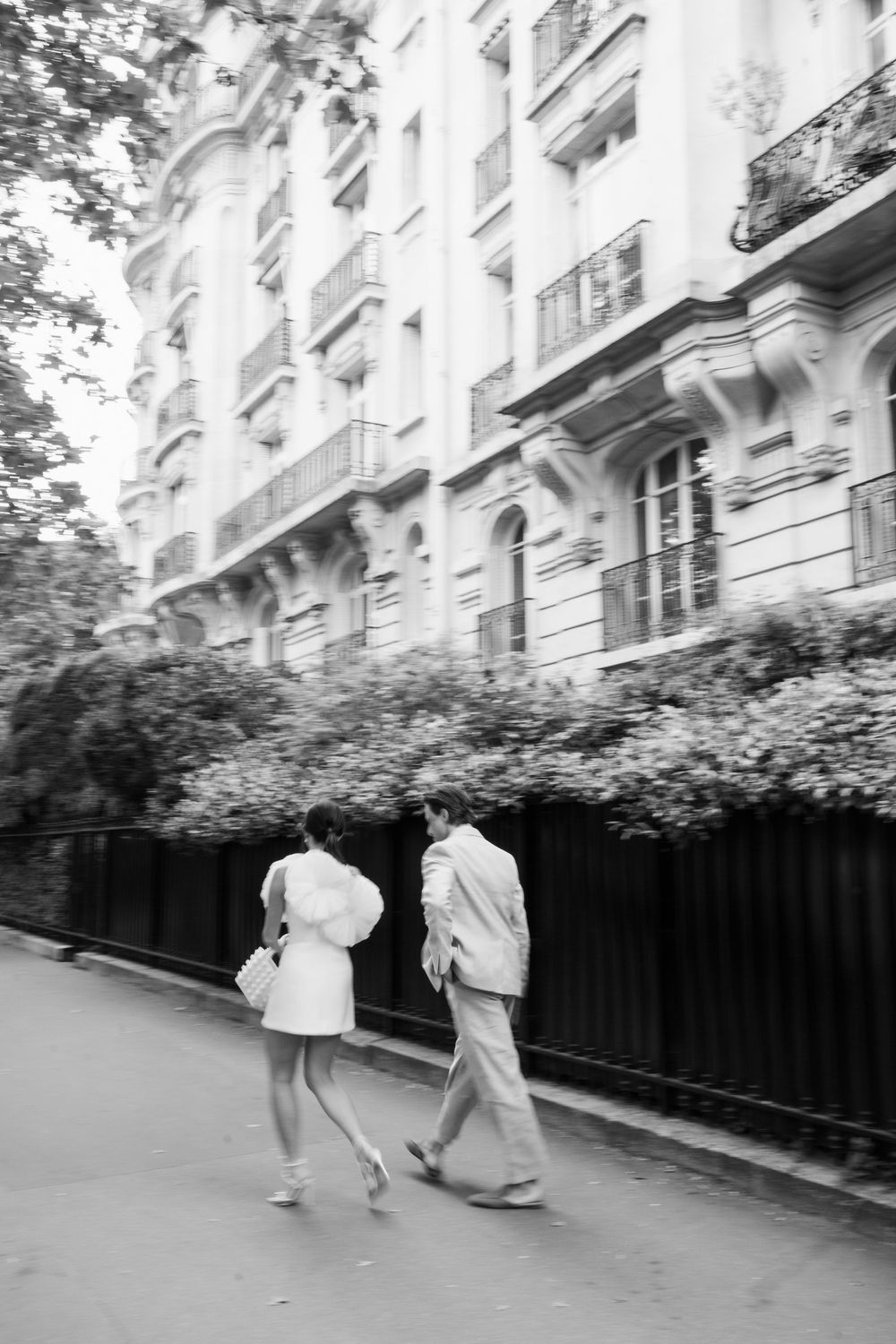 Black and white sequence shows people walking along a building's exterior wall in an artistic motion blur.