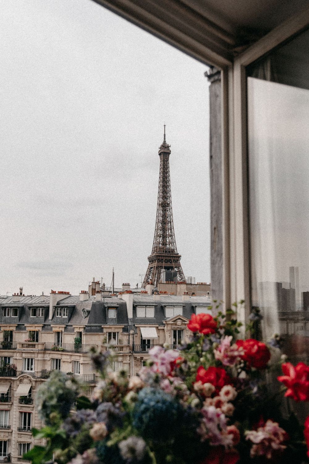 View of the Eiffel Tower from a Parisian balcony adorned with colorful flowers against an overcast sky.