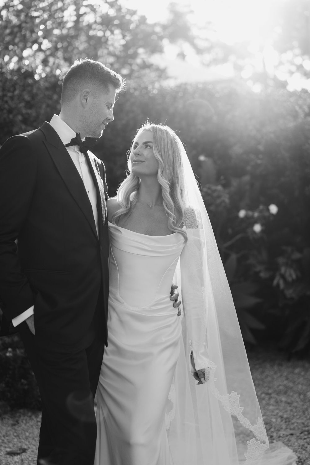 A romantic black and white wedding photo sequence shows a couple in backlit sunlight posing together in a garden setting.