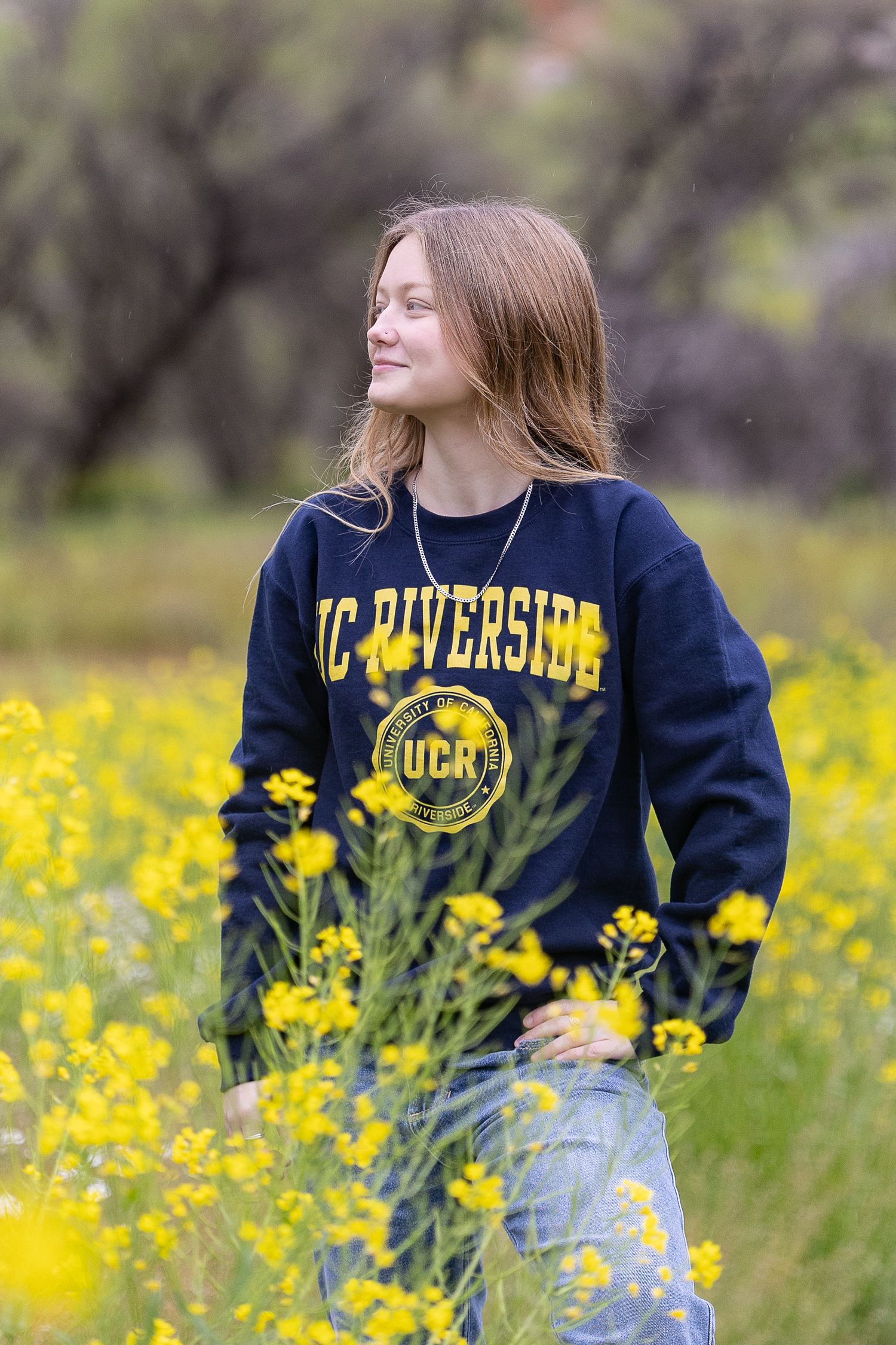 A person wearing a varsity letterman jacket poses against a wall with green foliage in the background.