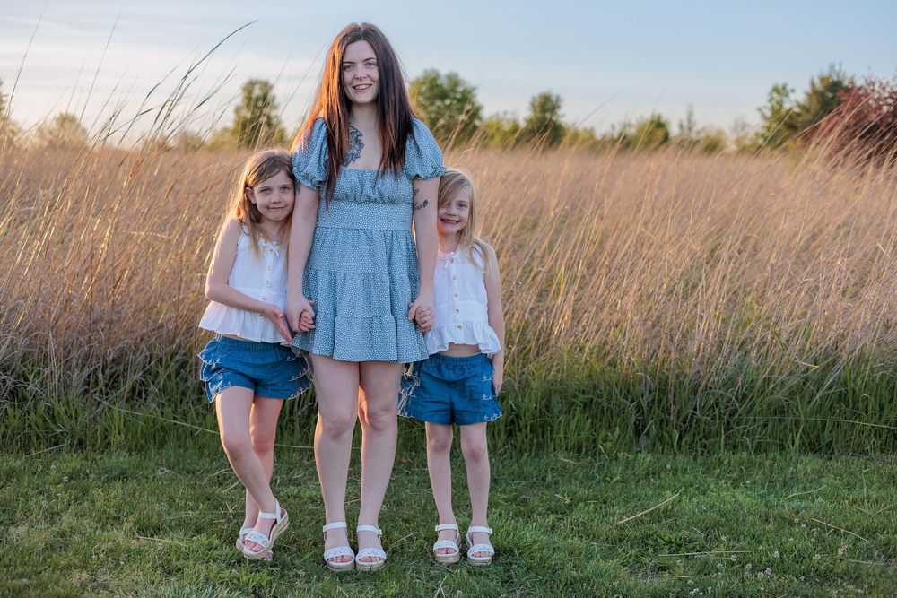 Three girls posing outdoors in a golden field at sunset, wearing denim shorts and white tops.