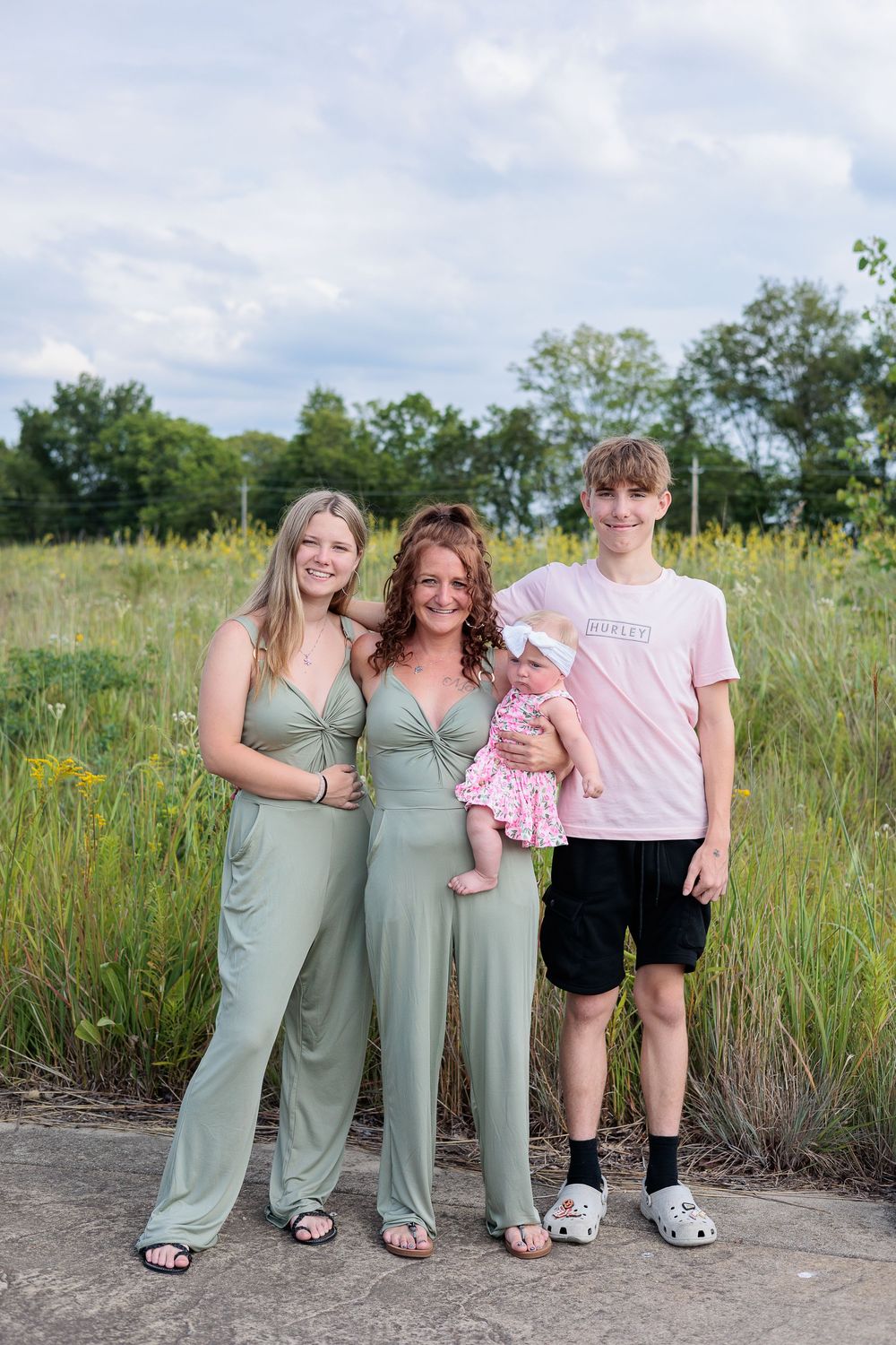 Family group wearing coordinated outfits poses together in a sunny meadow setting.