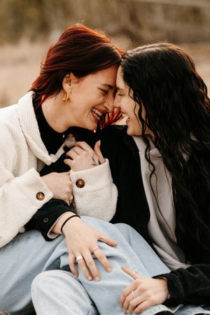 Two women laughing and embracing outdoors, sharing a joyful intimate moment together in casual winter attire.