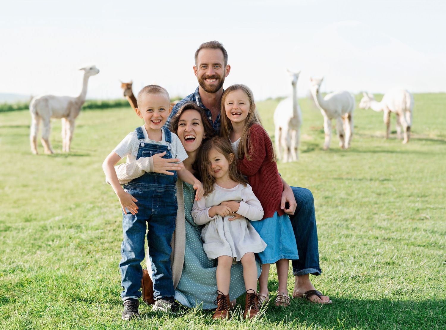 A family in front of a red barn with an alpaca.