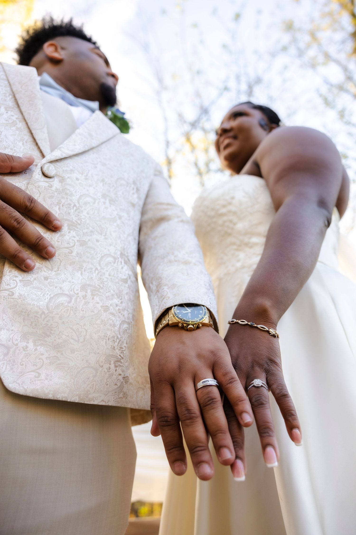 Close-up shot of newlyweds' hands showing off their wedding rings and formal attire.