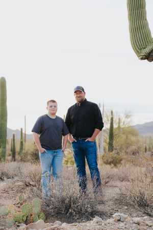 Three people standing in a desert landscape surrounded by towering saguaro cacti.