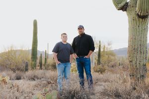 Desert landscape featuring people walking among giant saguaro cacti.