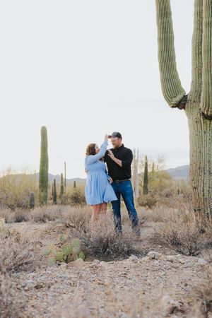 Intimate desert photoshoot with people embracing among towering saguaro cacti.