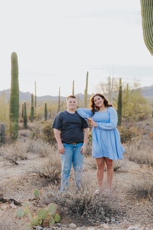 Group poses together in desert landscape surrounded by tall saguaro cacti during golden hour.