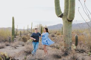 People walking through desert terrain with majestic saguaro cacti towering in background.