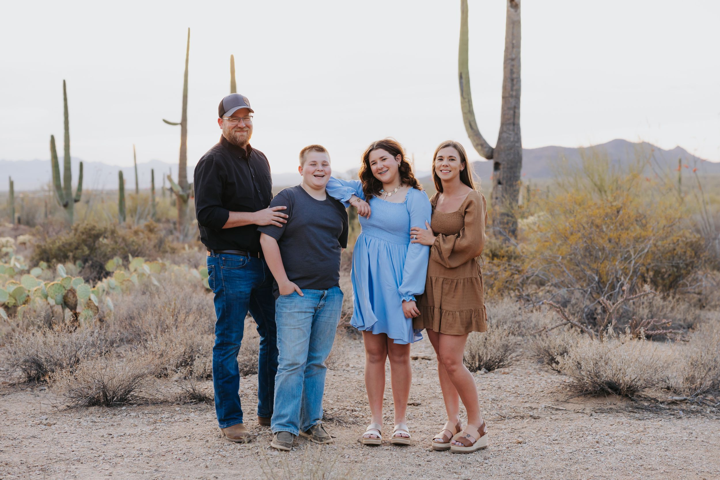 A couple poses in a desert landscape with saguaro cacti and mountains in the background.