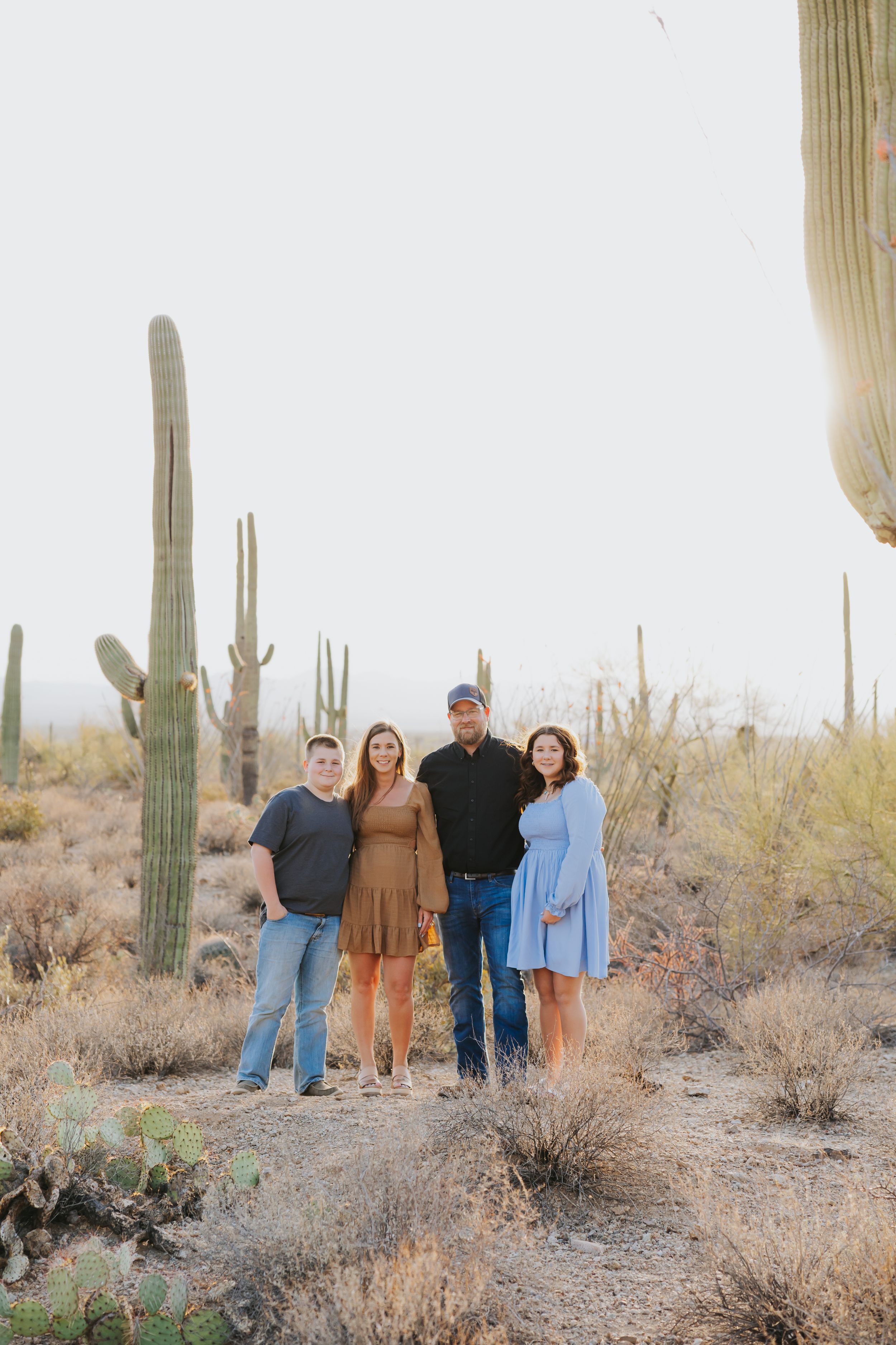 A group walks together through a desert landscape filled with tall saguaro cacti.
