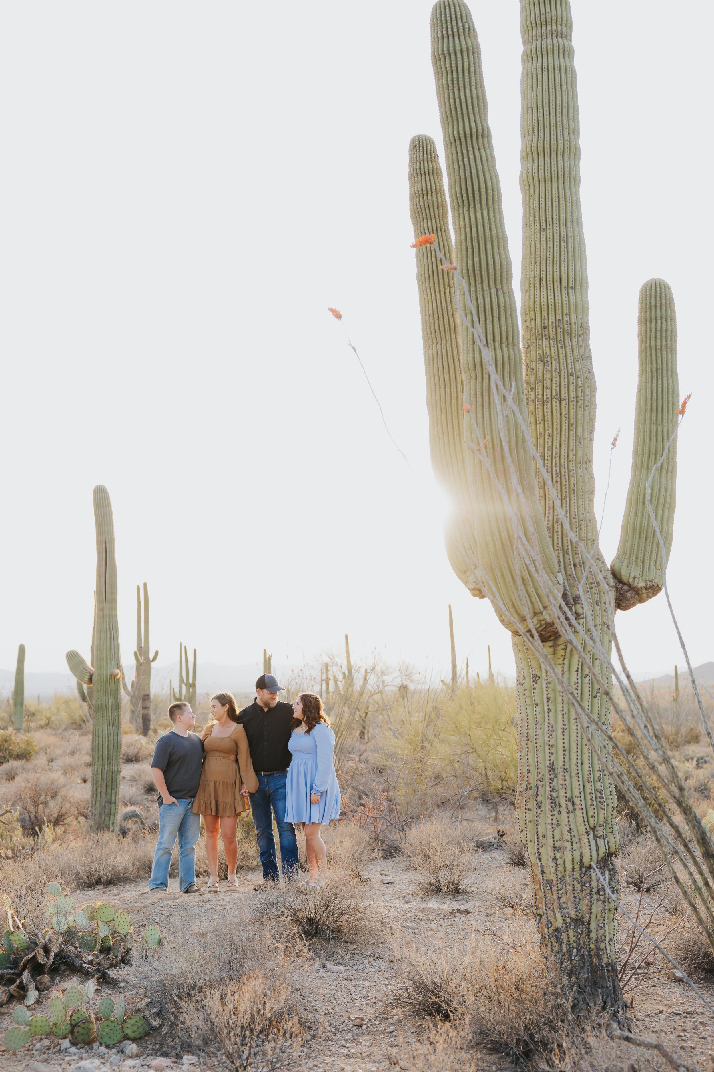People gather for a group photo among towering saguaro cacti in the desert.