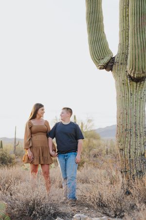 Couple walking through desert brush surrounded by giant saguaro cacti.