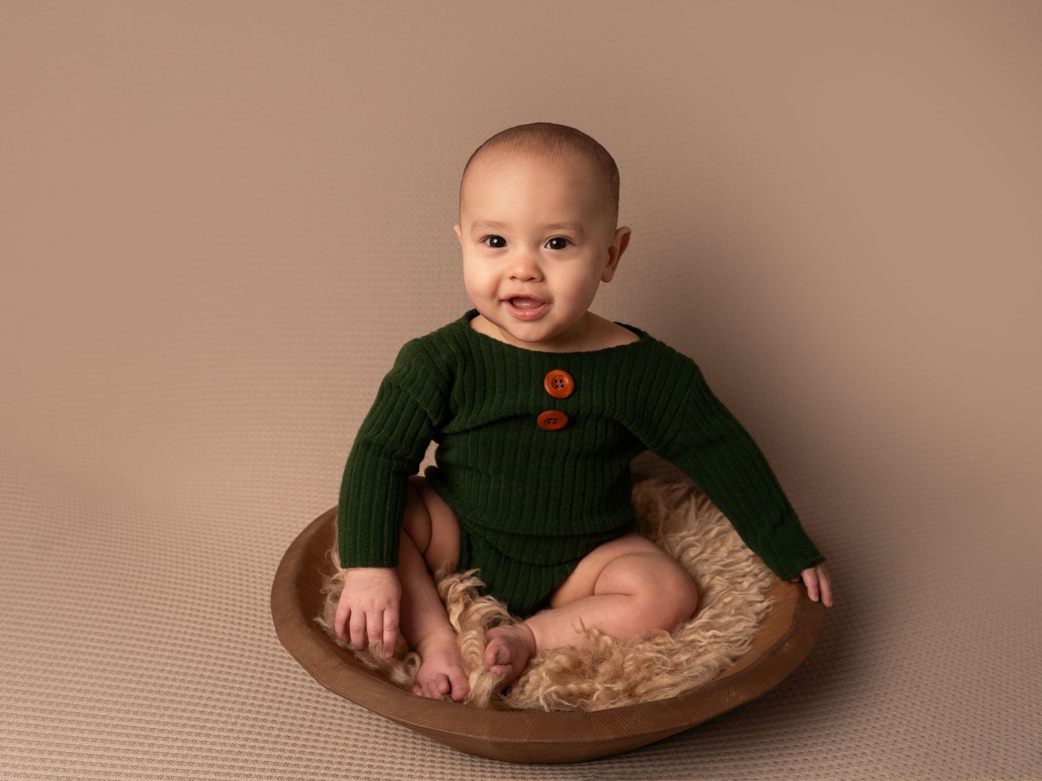 baby boy in green romper sitting in bowl prop on brown backdrop for sitter session by newborn photographer in doncaster.