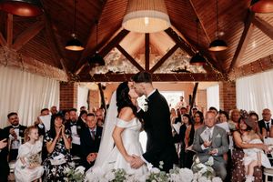 A romantic wedding ceremony captured inside a rustic wooden barn venue with white curtains and warm lighting.