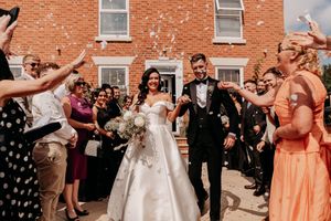Wedding guests enjoy a choreographed group dance moment during an outdoor celebration by a brick building.