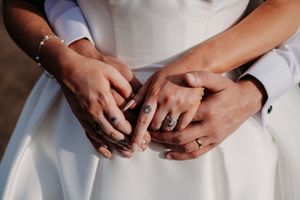 Close up of hands with wedding rings against white dress fabric showing affectionate details of a romantic moment.