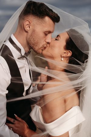 A tender wedding day kiss captured between newlyweds as the bride's veil flows delicately in the breeze.
