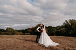 Wedding couple poses against dramatic cloudy sky on a golden field at sunset during their autumn celebration.