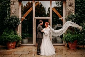 A romantic wedding scene in a stone courtyard with a flowing veil caught in the wind.