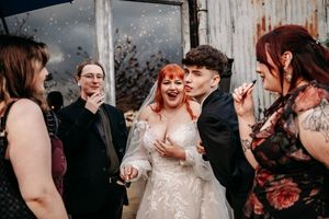 Wedding guests share joyful laughter with the bride during a candid reception moment with confetti falling.