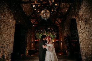A couple shares an intimate moment in a rustic stone-walled venue illuminated by warm lighting and disco balls.
