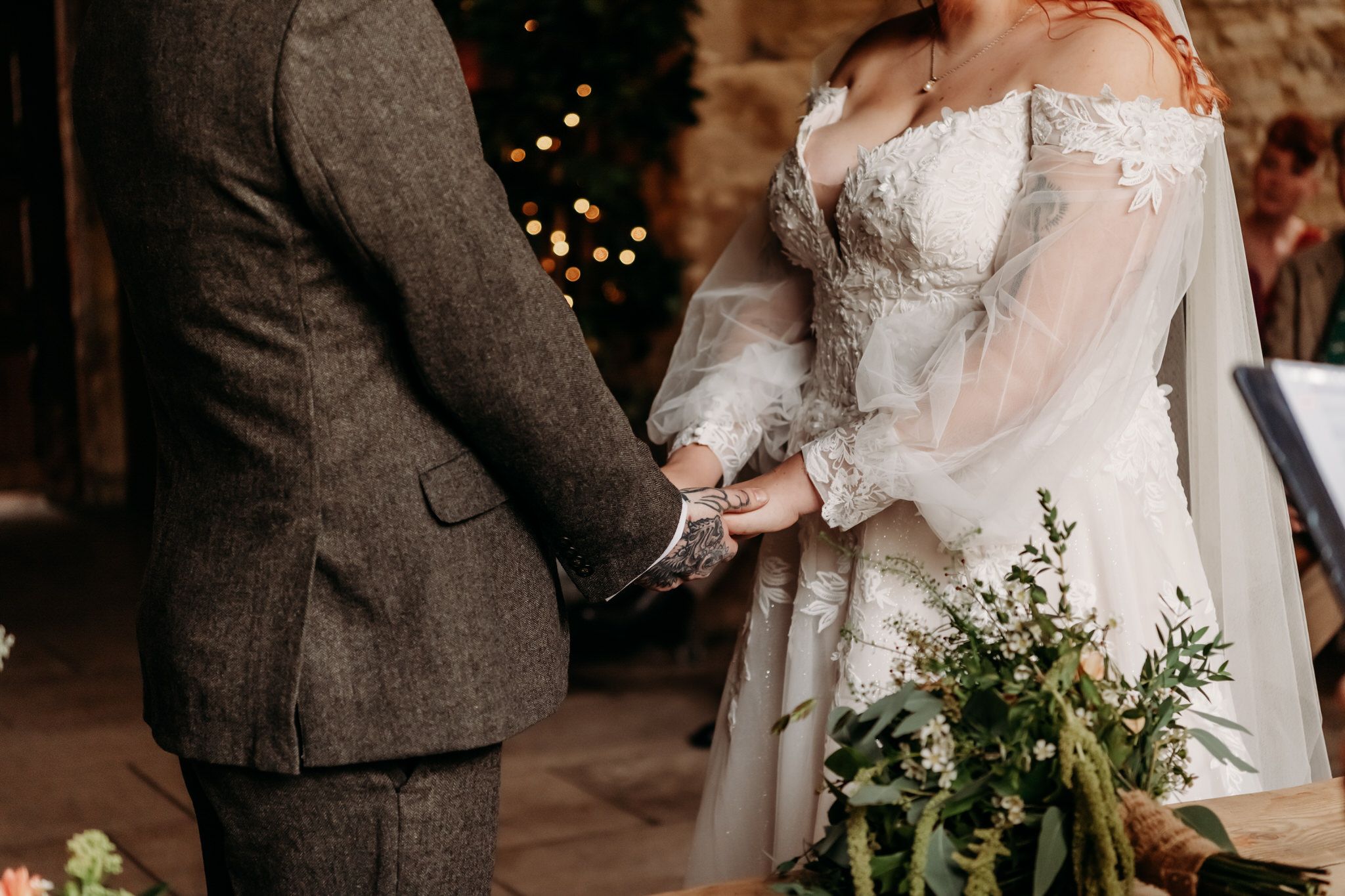 Elegant wedding couple embraces in a rustic barn venue with twinkling lights in the background.
