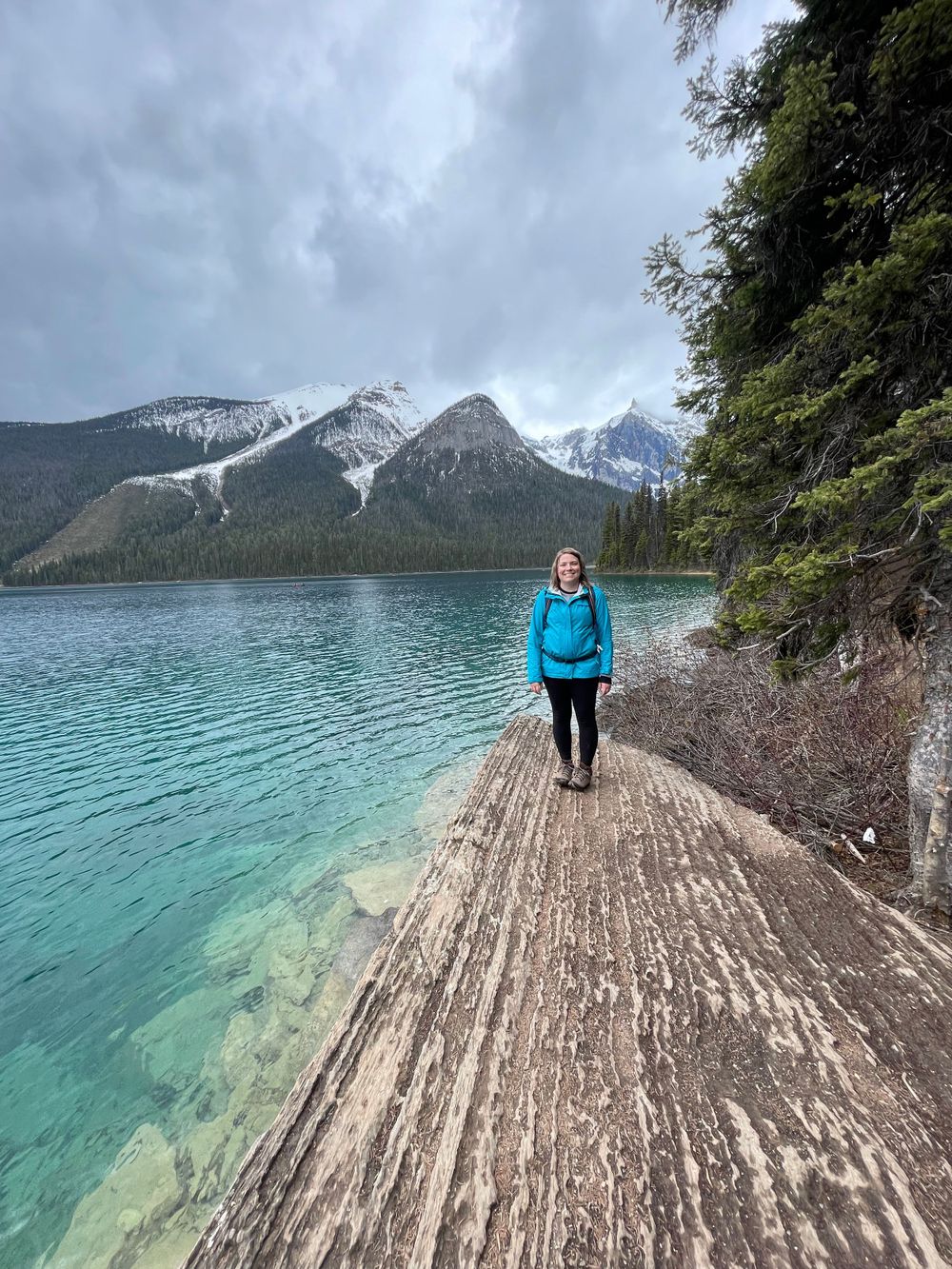a women stands on a rock by a turquoise lake with mountains in the background.