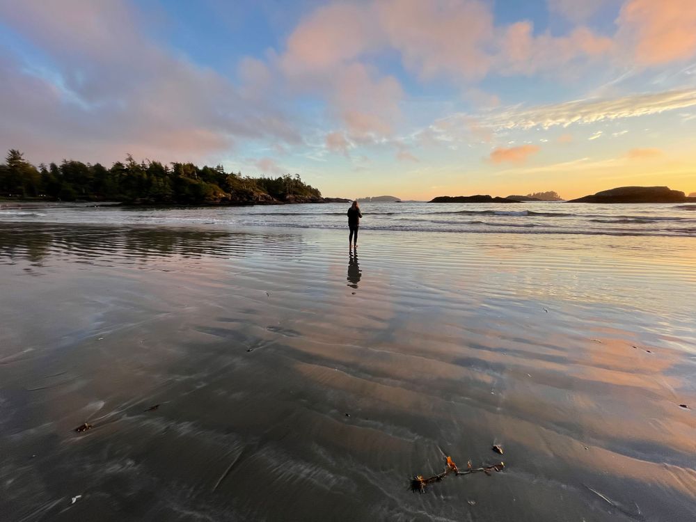 a women stands at a beach at sunset.