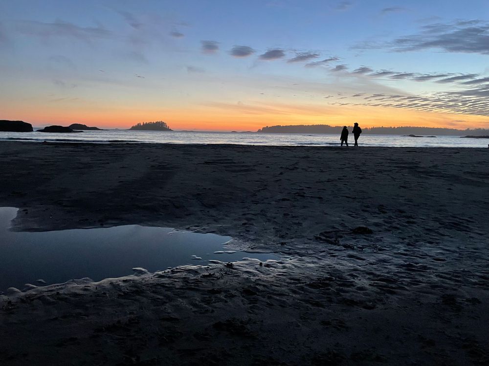 a couple walk along a beach at sunset.