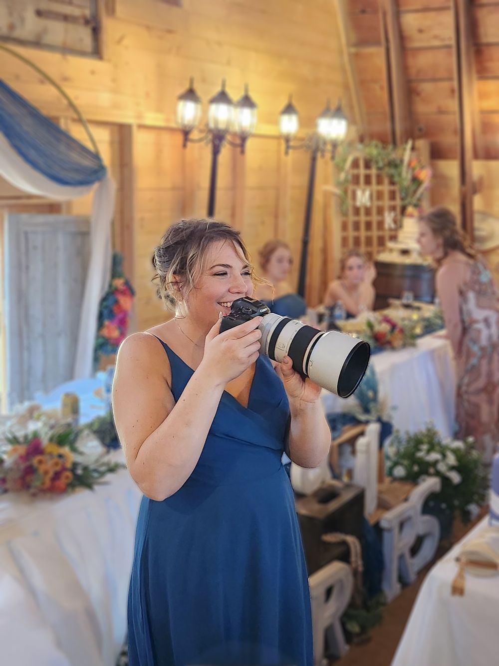 a women in a blue dress takes pictures with a large camera at at wedding.