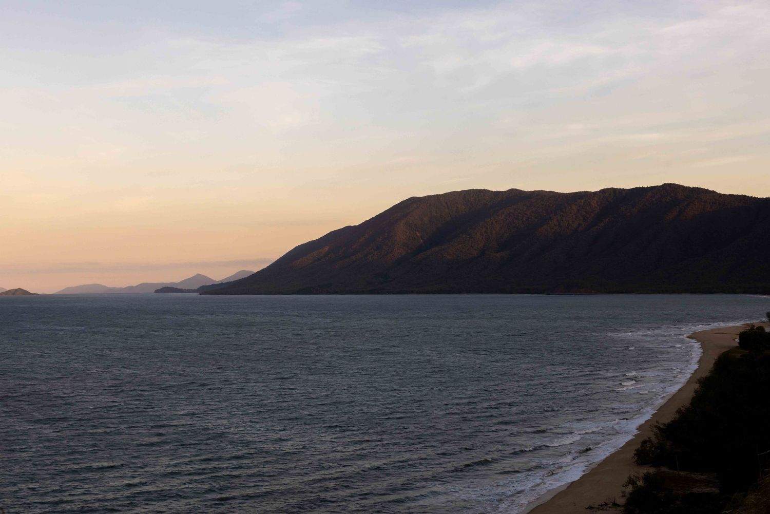 A scenic panoramic view of a coastal highway winding along rugged cliffs beside the ocean at sunset. Palm Cove Wedding