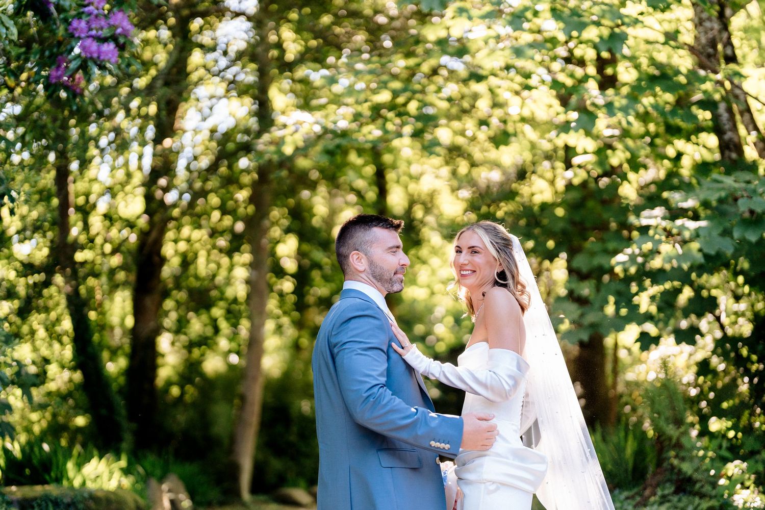 Couple embraces on a grassy hillside at sunset next to a majestic old cedar tree in a scenic countryside setting.