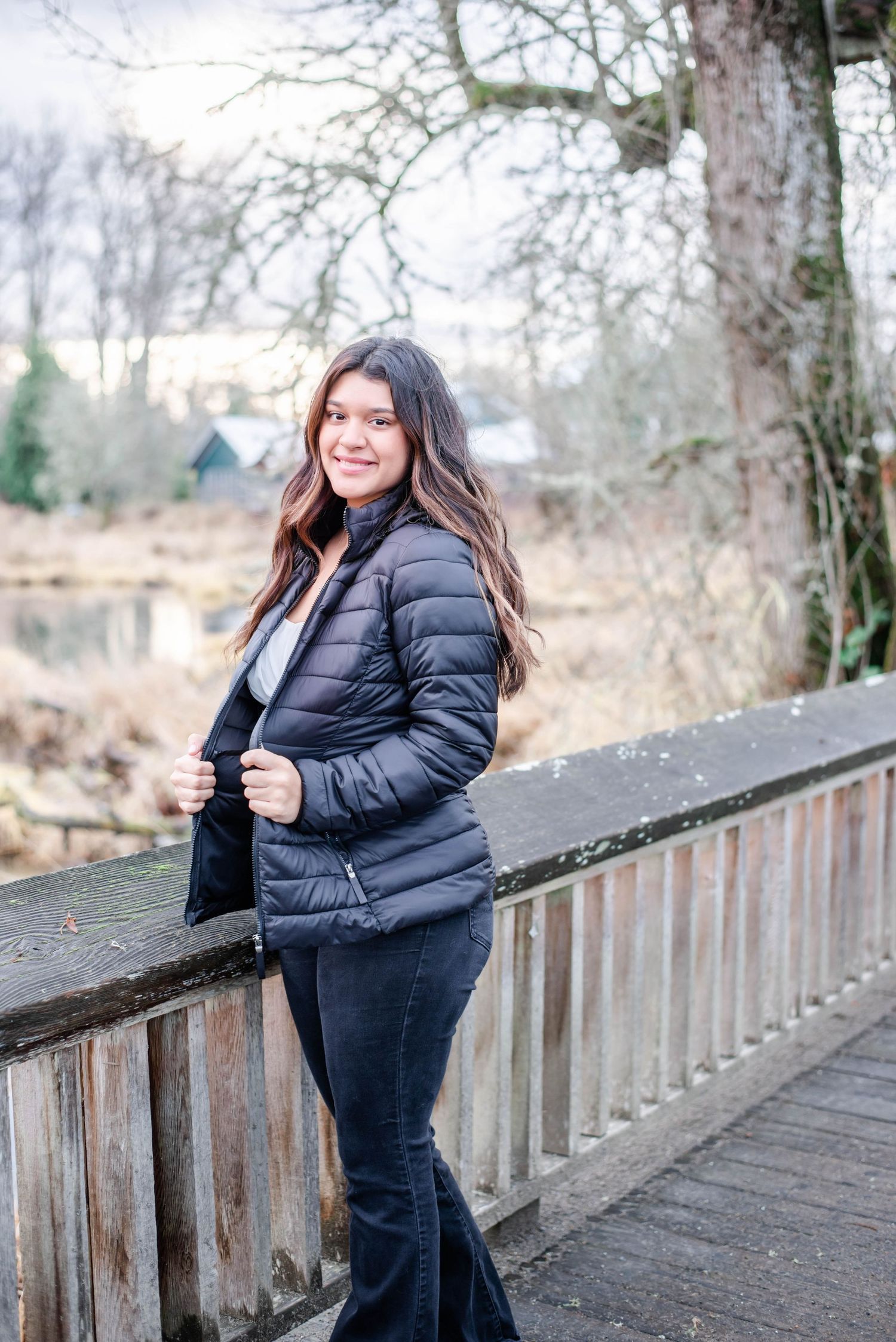 Person in black winter outfit poses on wooden bridge during winter season.