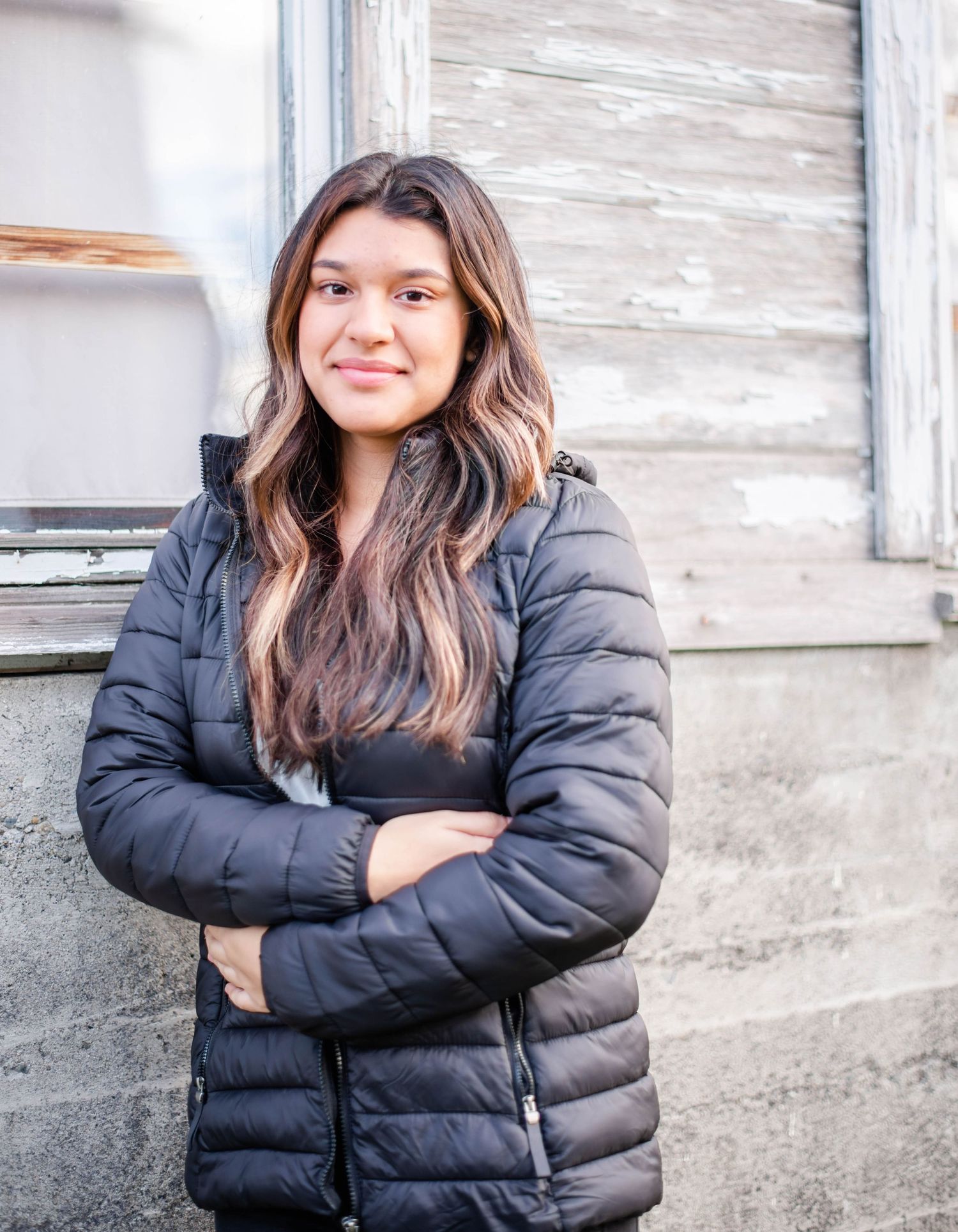 Figure wearing black puffer jacket stands confidently against weathered white wall.